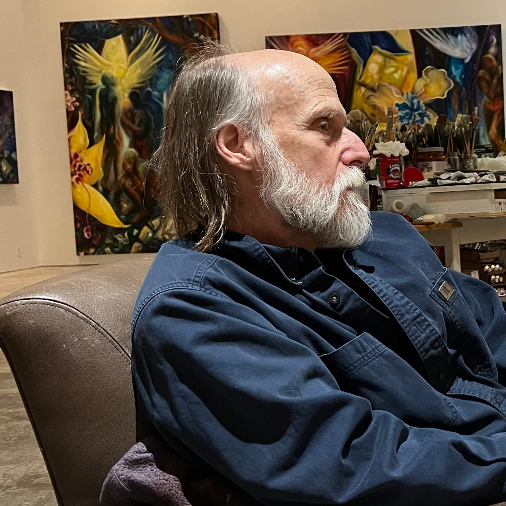 Jonathan D. Wallace seated in his Chicago studio, paintings on the wall behind him